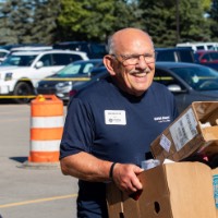 Class of 1967 Alumnus smiles as he carries in 2 cardboard boxes for new lakers